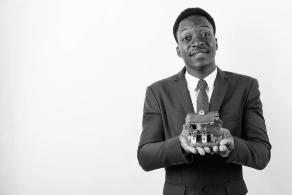 Молодий гарний африканський комерсант тримає фігурку будинку на білому фоні. — стокове фото