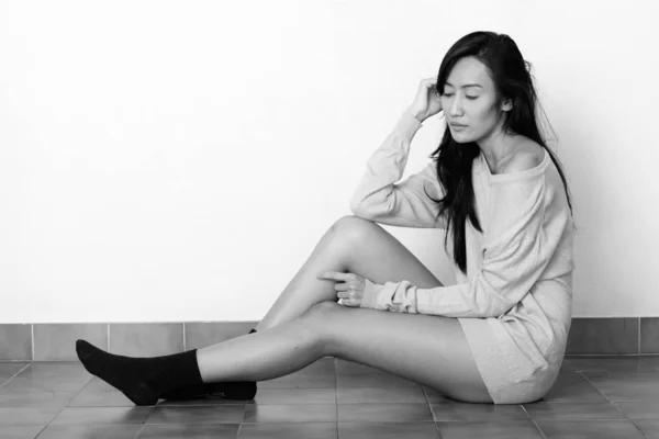Studio shot de joven hermosa mujer asiática sentada en el suelo con los ojos cerrados —  Fotos de Stock
