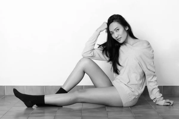 Studio plan de jeune belle femme asiatique assise sur le sol tout en se penchant sur la main — Photo