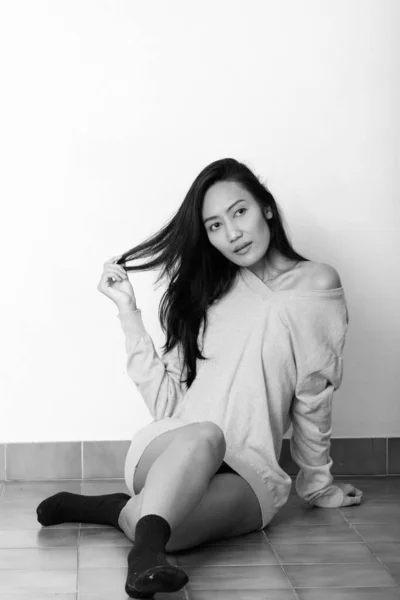 젊고 아름다운 아시아 여성 이 머리를 갖고 놀다가 바닥에 앉아 생각하는 모습을 스튜디오에서 촬영 — 스톡 사진