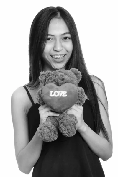 Joven feliz asiática adolescente sonriendo mientras sostiene oso de peluche con corazón y amor signo —  Fotos de Stock