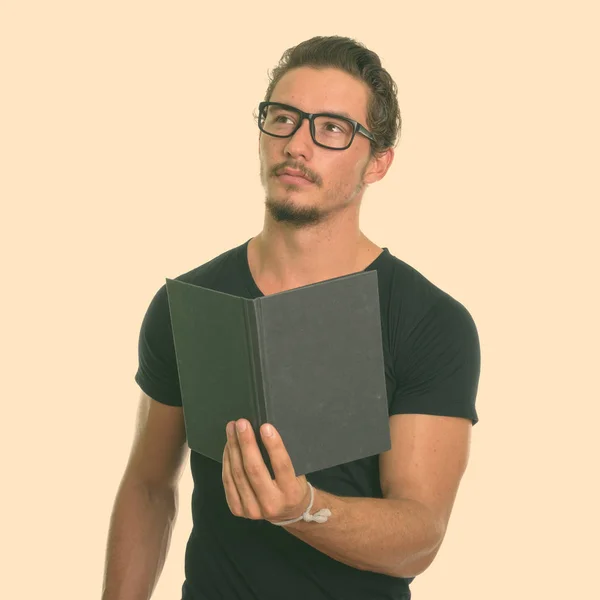 Studio shot of young handsome man holding book while thinking with eyeglasses isolated against white background
