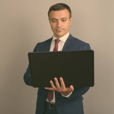 Gri arka planı dizüstü tutarken takım giyen işadamı stüdyo çekim