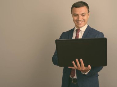 Gri arka planı dizüstü tutarken takım giyen işadamı stüdyo çekim