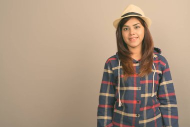 Gömlek ve gri arka plan karşı şapka giyen genç güzel Hintli turist kadın Studio atış kontrol