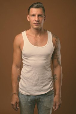 Kahverengi arka plan beyaz kolsuz bluz giyen kaslı adam stüdyo çekim