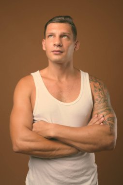Kahverengi arka plan beyaz kolsuz bluz giyen kaslı adam stüdyo çekim
