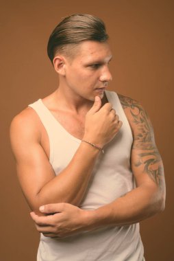 Kahverengi arka plan beyaz kolsuz bluz giyen kaslı adam stüdyo çekim