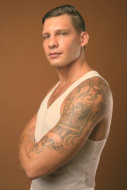 Kahverengi arka plan beyaz kolsuz bluz giyen kaslı adam stüdyo çekim
