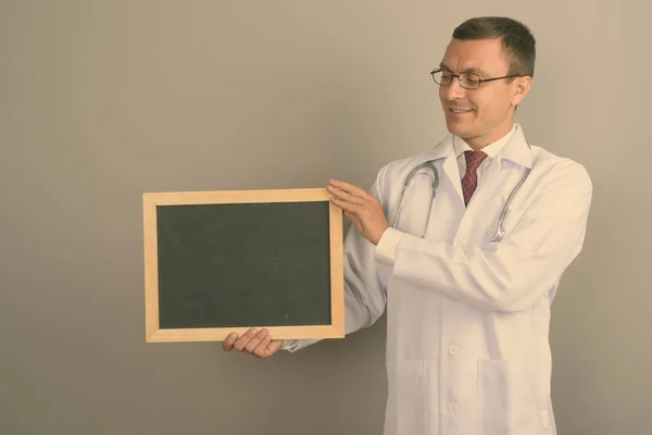 工作室拍摄的男子医生戴眼镜 而持有黑板反对灰色背景 — 图库照片