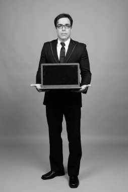 Studio shot of handsome Persian businessman against gray background in black and white