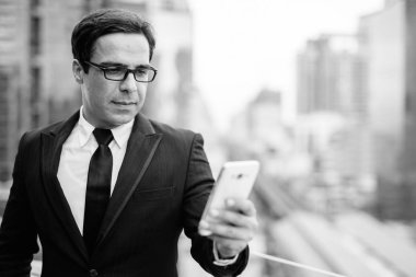 Portrait of handsome Persian businessman against view of Bangkok city in black and white
