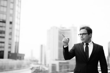 Portrait of handsome Persian businessman against view of Bangkok city in black and white