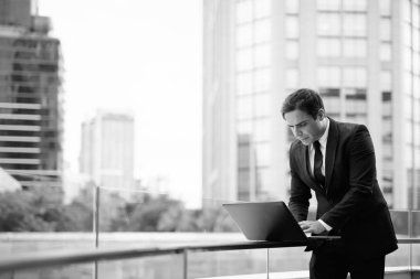 Portrait of handsome Persian businessman against view of Bangkok city in black and white