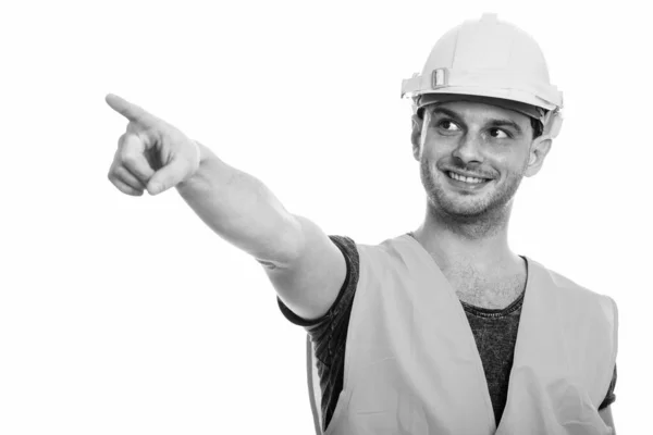 Estudio de tiro de joven feliz hombre trabajador de la construcción sonriendo mientras señala el dedo — Foto de Stock