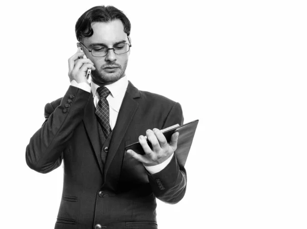 Studio shot of young businessman talking on mobile phone while reading on clipboard Royalty Free Stock Images