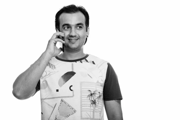 Studio shot of happy Persian man smiling and talking on mobile phone while thinking — Stock Photo, Image