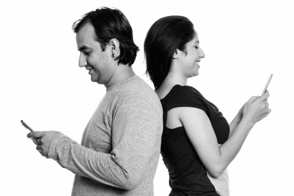 Щаслива пара Перська, посміхаючись під час використання мобільного телефону разом спина до спини — стокове фото