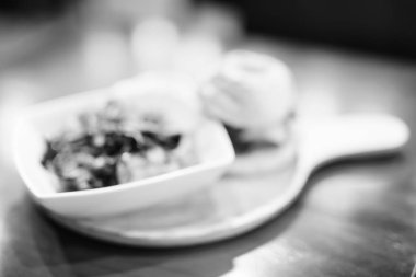 Defocused Shot Of Blurred Cheeseburger And Salad Served On Wooden Table In Black And White