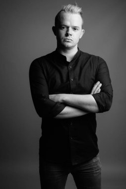 Studio shot of businessman with Mohawk hairstyle and blond hair against gray background in black and white