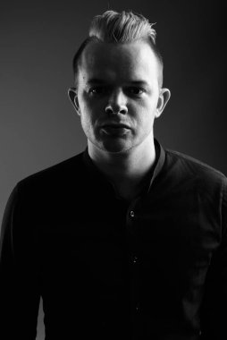 Studio shot of businessman with Mohawk hairstyle and blond hair against gray background in black and white