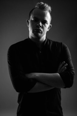 Studio shot of businessman with Mohawk hairstyle and blond hair against gray background in black and white