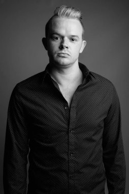 Studio shot of businessman with Mohawk hairstyle and blond hair against gray background in black and white