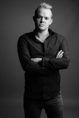 Studio shot of businessman with Mohawk hairstyle and blond hair against gray background in black and white