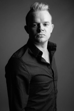 Studio shot of businessman with Mohawk hairstyle and blond hair against gray background in black and white
