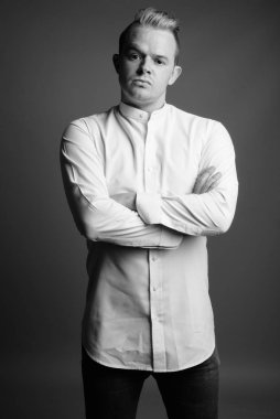 Studio shot of businessman with Mohawk hairstyle and blond hair against gray background in black and white