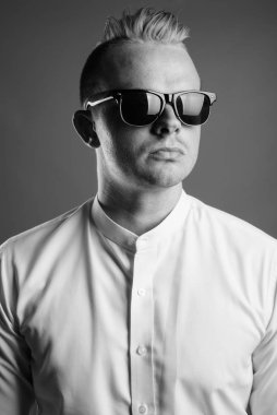 Studio shot of businessman with Mohawk hairstyle and blond hair against gray background in black and white