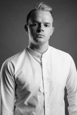 Studio shot of businessman with Mohawk hairstyle and blond hair against gray background in black and white