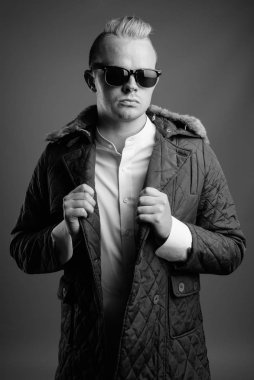 Studio shot of man with Mohawk hairstyle and blond hair against gray background in black and white