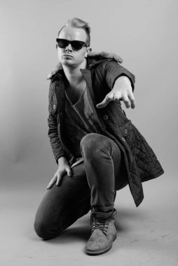 Studio shot of man with Mohawk hairstyle and blond hair against gray background in black and white