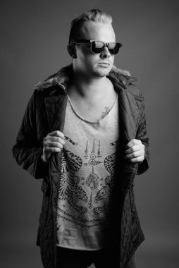 Studio shot of man with Mohawk hairstyle and blond hair against gray background in black and white