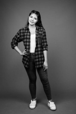 Studio shot of young beautiful Asian hipster woman against gray background in black and white