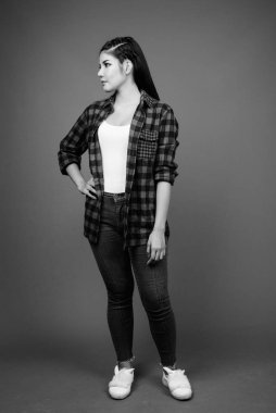 Studio shot of young beautiful Asian hipster woman against gray background in black and white