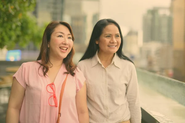 Dos mujeres asiáticas maduras juntas contra la vista de la ciudad — Foto de Stock
