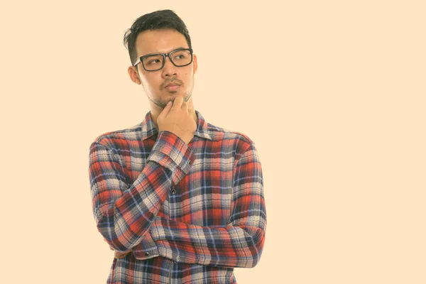 Studio shot of young Asian man thinking while wearing eyeglasses — Stock Photo, Image