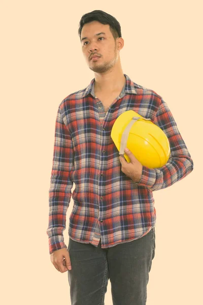Зйомки молодого азіатського будівельника, який стоїть і думає, зберігаючи шолом безпеки. — стокове фото