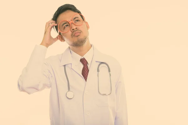 Estúdio tiro de jovem asiático homem médico pensando enquanto coça a cabeça — Fotografia de Stock