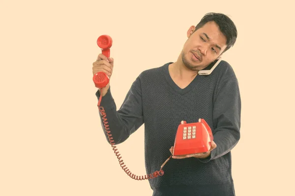 Stúdió lövés fiatal ázsiai férfi ad régi telefon, miközben beszél a mobiltelefon — Stock Fotó