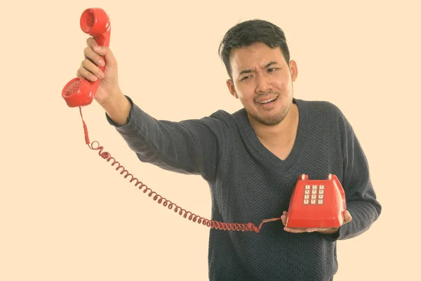 Estúdio tiro de jovem asiático homem segurando telefone velho olhando chateado — Fotografia de Stock