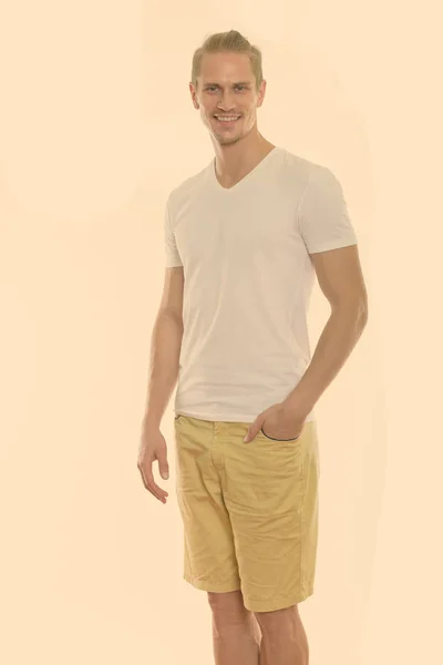 Studio shot of happy young handsome man smiling while standing with hand on pocket — Stock Photo, Image