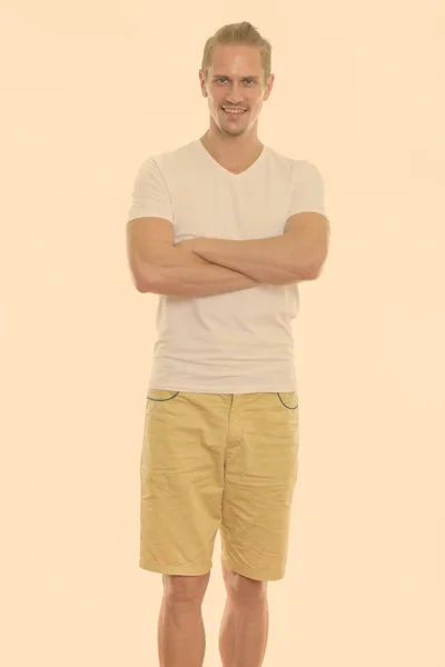 Studio shot of happy young handsome man smiling and standing with arms crossed — Stock Photo, Image