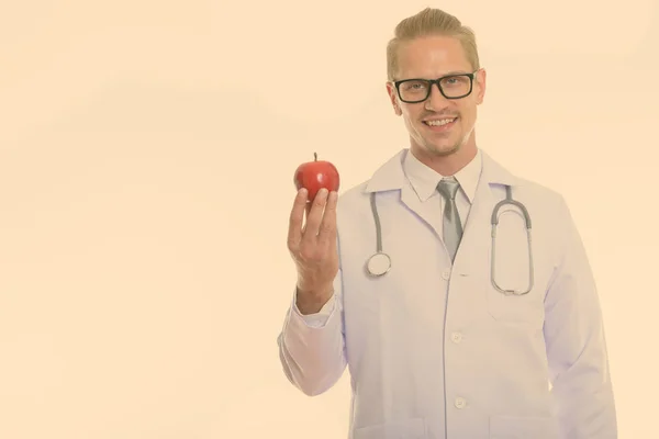 Студійний знімок щасливого молодого красивого лікаря, який посміхається, тримаючи червоне яблуко — стокове фото