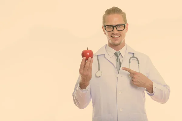 Щасливий молодий красивий чоловік лікар посміхається, тримаючись і вказуючи на червоне яблуко — стокове фото