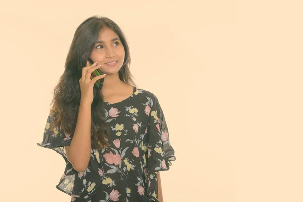 Estúdio tiro de jovem feliz mulher persa sorrindo e pensando ao falar no telefone celular isolado contra fundo branco — Fotografia de Stock