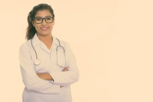 Estúdio tiro de jovem feliz mulher persa médico sorrindo enquanto vestindo óculos com braços cruzados isolado contra fundo branco — Fotografia de Stock