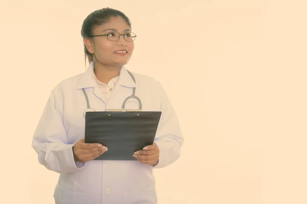 Estudio de la joven feliz mujer persa gorda médico sonriendo y pensando mientras sostiene portapapeles aislado sobre fondo blanco — Foto de Stock